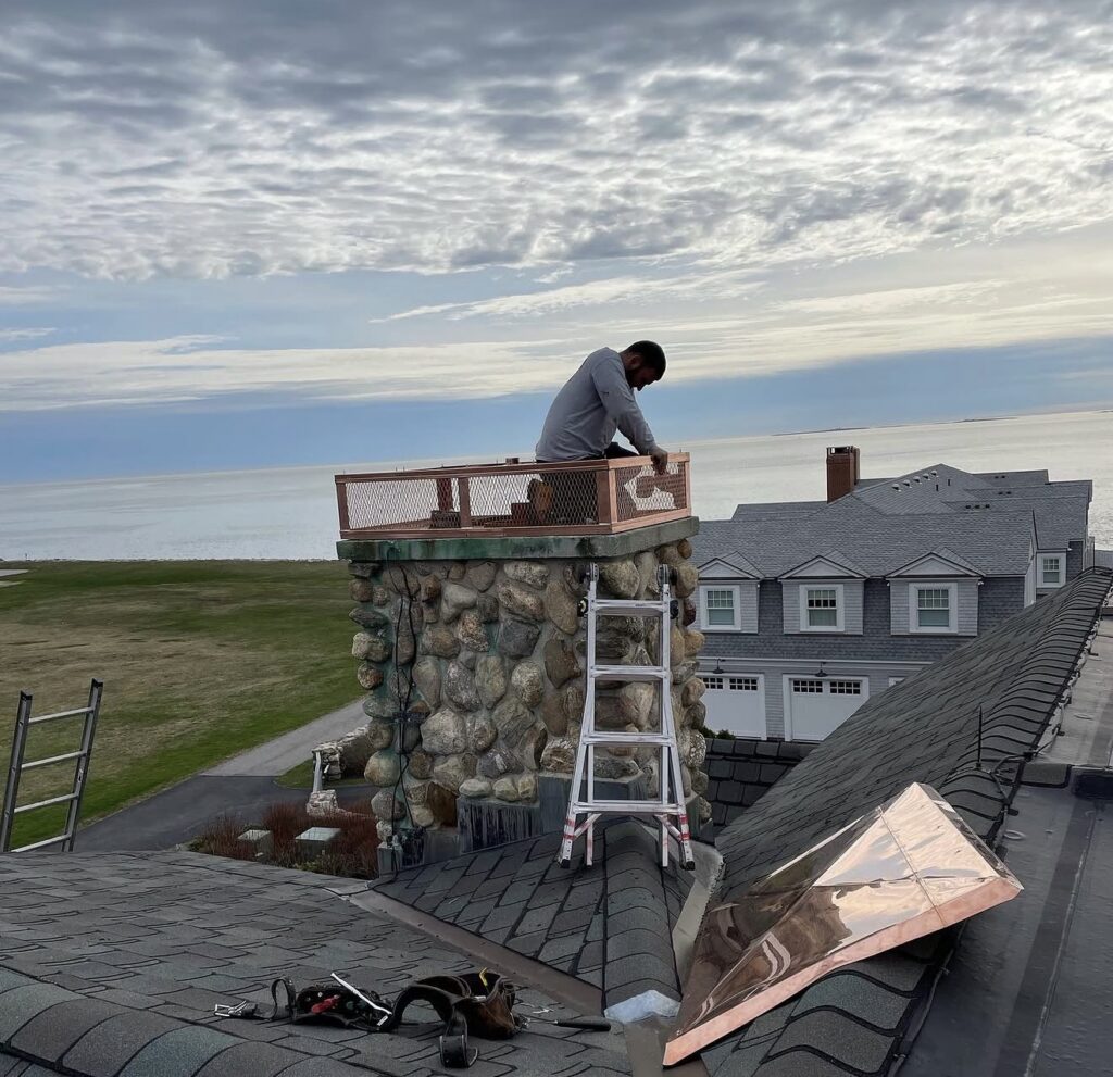 Paul John & Son craftsman installing a custom copper chimney cap on an oceanfront luxury home in coastal Massachusetts