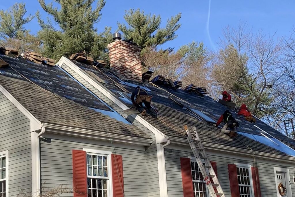 Installing-asphalt-certainteed-shingles-ma (1) Paul John & Son roofing crew installing CertainTeed Landmark asphalt shingles on a Cape Cod style home — full roof replacement in Greater Boston