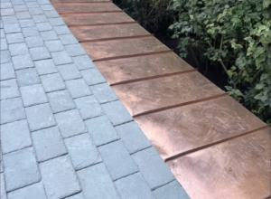 Custom fabricated copper standing seam roof section meeting a slate roof on the same plane, detail of material transition