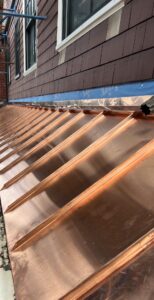 Bright new copper standing seam roofing on a cedar shake home in Massachusetts, custom fabricated by Paul John & Son
