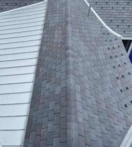 DaVinci composite slate roof meeting aluminum standing seam metal at the hip ridge of a large estate home in Concord, MA — clean transition with custom flashing, slate snow guards visible across the slate field.